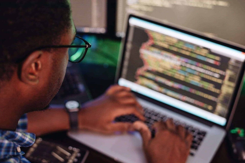 Schwarzer Mann vor dem Computerbildschirm, der mobile App, Webentwicklung, Computerprogrammierung kodiert